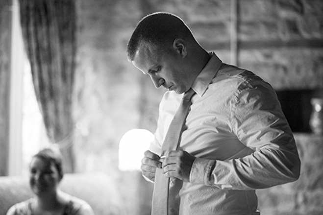 black and white of groom getting dressed