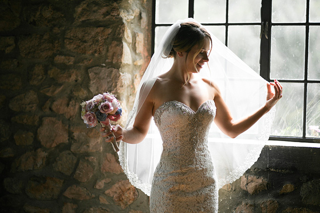 Happy bride holding veil by window